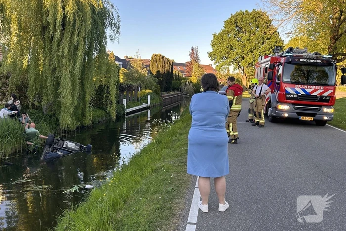 Auto belandt op de kop in het water, omstanders verrichten redding