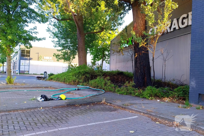 Brand in boom en bosschages naast bedrijfspand