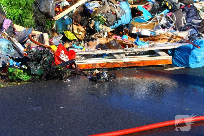 Grote afvalcontainer met huisvuil vat vlam tijdens rit