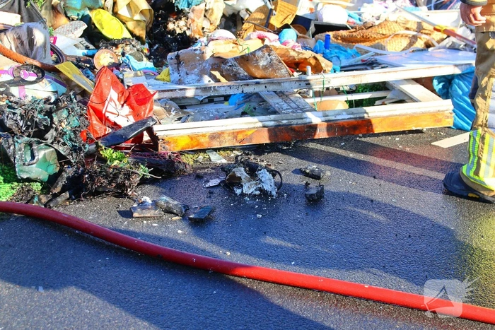 Grote afvalcontainer met huisvuil vat vlam tijdens rit