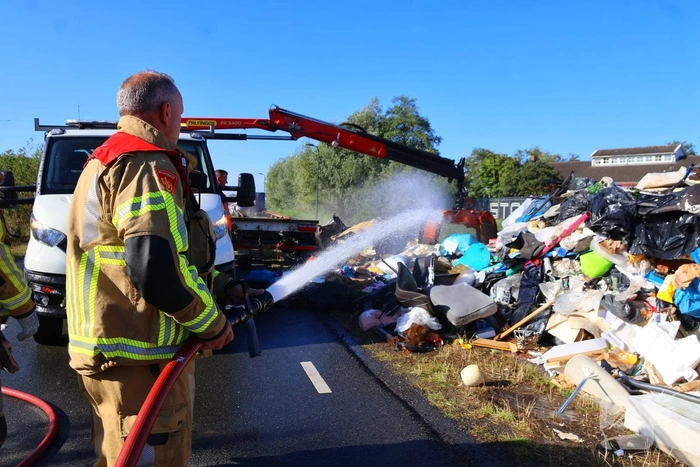 Grote afvalcontainer met huisvuil vat vlam tijdens rit