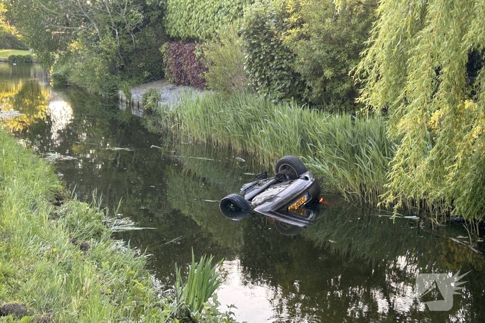 Auto belandt op de kop in het water, omstanders verrichten redding