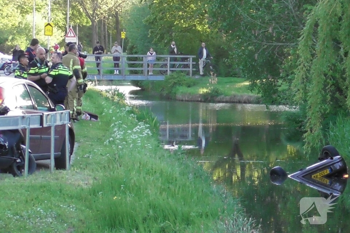 Auto belandt op de kop in het water, omstanders verrichten redding